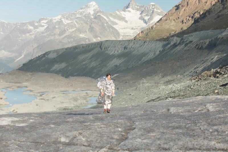 Anne-Sophie Balzer stands on the glacier ice in the wind, wrapped in a rescue blanket with the golden side facing outwards